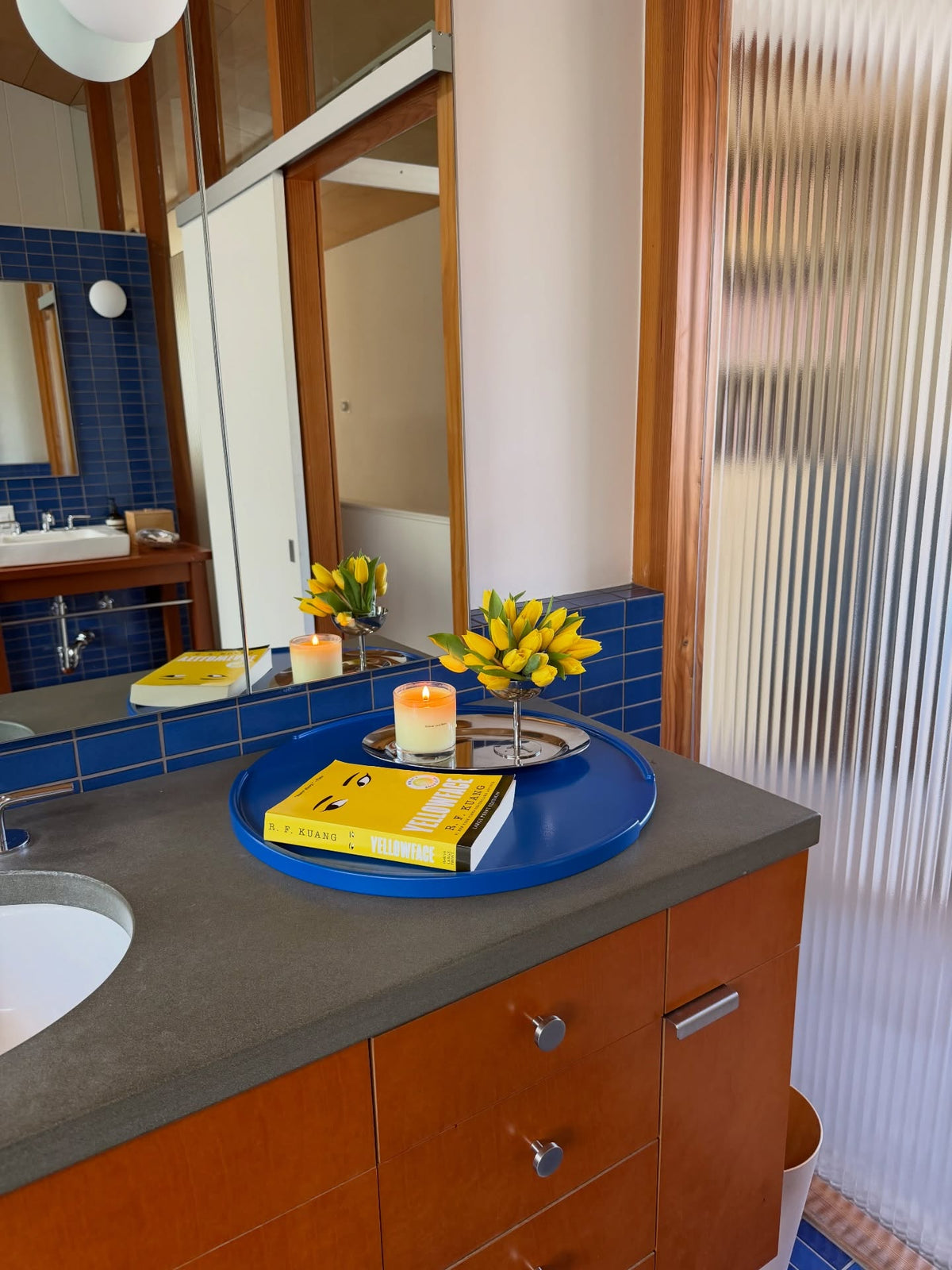 a new tradition oval tray with yellow flowers and a candle on the blue tile bathroom ledge